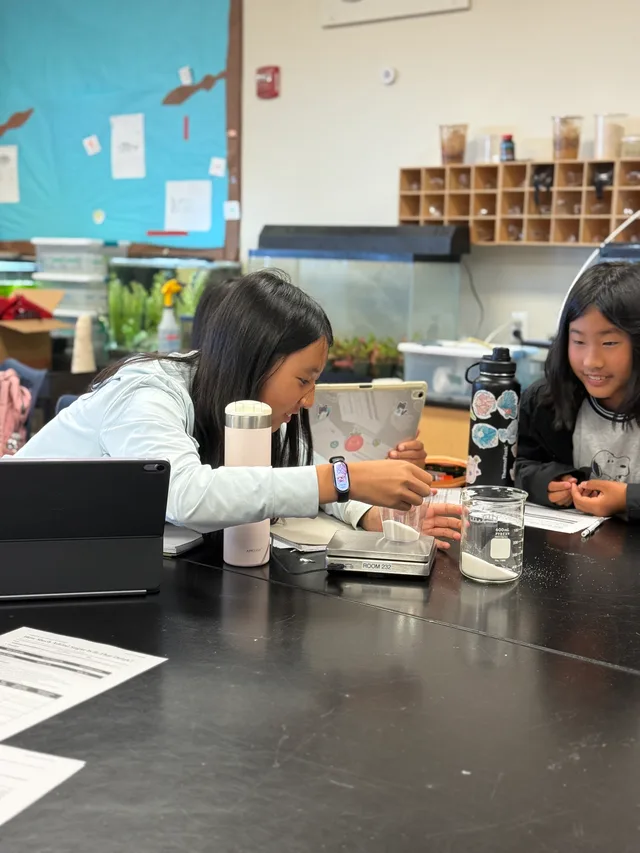 Two students use a digital scale to measure sugar during a school workshop
