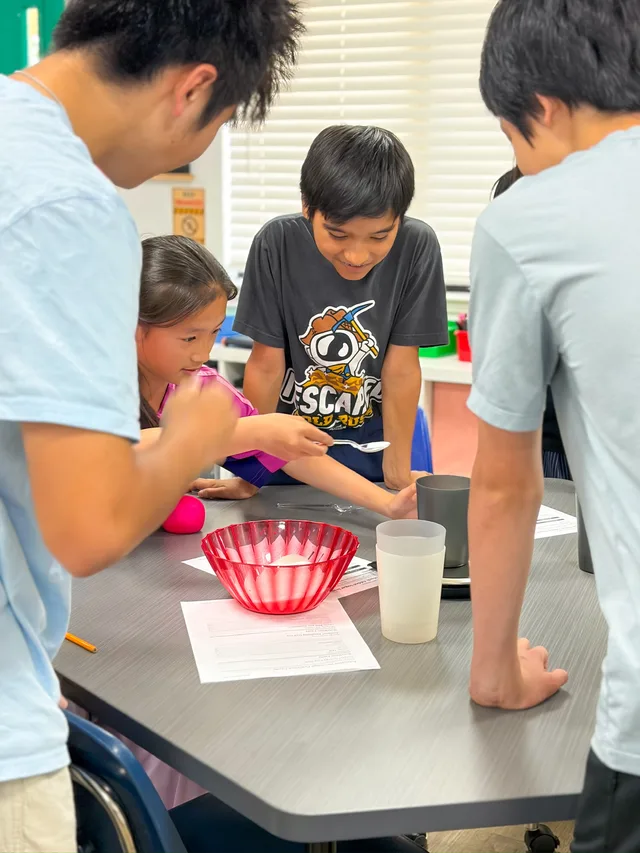 Workshop leaders and students gather around a table to measure sugar into cups